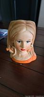 Front view of glazed porcelain female head figurine with orange collar and bows
