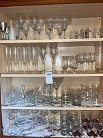 Three shelves of assorted clear glass and crystal stemware and tumblers in cabinet