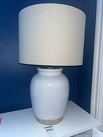 Front view of white ceramic table lamp with beige drum shade