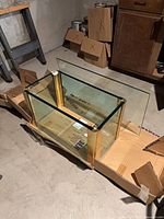 overall view of glass and brass-tone table base with glass top panel leaning nearby