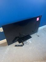 Front view of JVC 48-inch TV with remote, cables and Fire Stick on floor