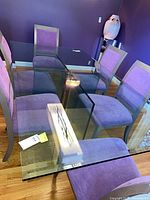 Full view of glass dining table with clear top and purple chairs around for scale