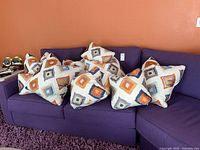All eight pillows grouped on purple sofa showing pattern and quantity