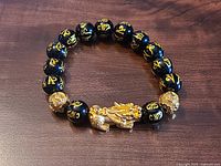 Full view of bracelet showing black beads with gold script and central Pi Xiu charm