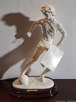 Front view of alabaster soccer player statue on wood base with tag visible