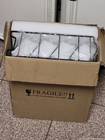 Cardboard box containing black metal rack and foam-protected glass jars