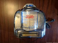 Front view showing Pepsi-Cola jukebox with selector panel and power cord