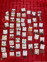Full layout of approximately 50 pairs of earrings on red surface