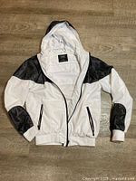 Front view of CSG white jacket showing hood, black mesh panels, zip pockets, ribbed cuffs