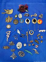 Complete lot overview displaying 39 brooches and pins on blue cloth