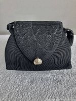 Front view of black corded handbag with shell clasp and swirl flap design
