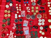 Wide view of assorted buttons laid out on red cloth showing variety of colors, sizes and materials