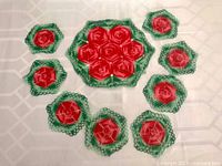 Overhead view of nine crocheted doilies: one large centerpiece surrounded by eight smaller matching coasters, red and green color scheme