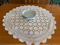 Full view of round white crochet doily on table with bowl for scale