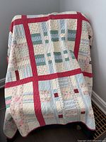 Front view of full quilt draped, shows red sashing and multicolour blocks
