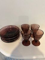 Stack of four purple plates alongside four purple stemmed glasses