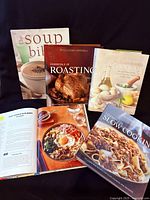 Front covers of five cookbooks, four standing one open, showing titles and illustrations