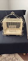 Front view of cream metal bird cage with ornate scrollwork