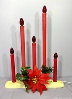 Front view of 5-light red plastic candelabra on cream base with greenery and poinsettia