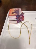 Single ornament displaying book stack with gold cord