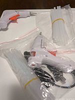 Two white mini hot glue guns with cords and bundled clear glue sticks in plastic bags