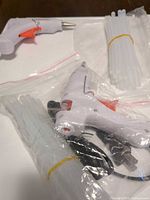 Two white mini hot glue guns, one bagged, with bundled clear glue sticks