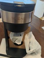 Front view of coffee maker showing stainless accent, drip area and protective plastic