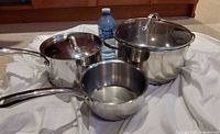 Three stainless steel pots displayed together, two with lids