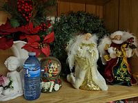 Shelf view showing wreath, two angel figures, snow globe, cherub, vase with poinsettias