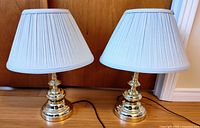 Pair of brass-tone table lamps with pleated shades shown side by side on floor, cords visible