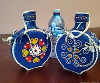 Front view of both blue leather-wrapped canteens next to water bottle for scale