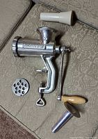 Complete meat grinder assembled with crank, two plates and two funnels displayed on sofa