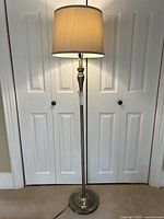 Full view of brass-tone floor lamp with shade illuminated