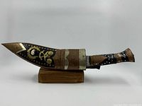 Left profile of kukri in sheath on stand showing brass and copper mounts