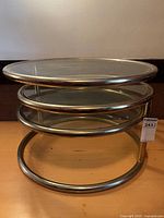 Front view of table collapsed showing three glass tiers within brass-tone rings