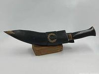 Kukri in scabbard on wood stand, side view
