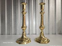 Front view of both polished brass candlesticks on white surface