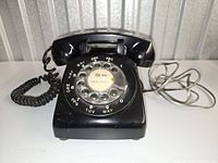 Front angle of black Northern Electric rotary phone showing rotary dial, handset, cords