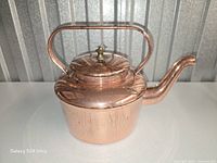 Profile view of copper tea pot showing body, handle, lid, spout