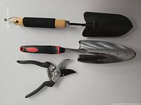 All three garden tools laid out: pruning shears, stainless trowel, black trowel
