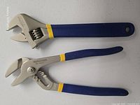Adjustable wrench above tongue-and-groove pliers, blue grips visible