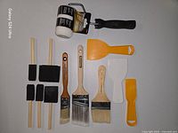 All items laid out: 3 bristle brushes, 4 foam brushes, roller frame with cover, 3 scrapers