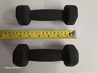 Top-down view of both dumbbells beside measuring tape showing approx length