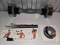 Shake Weight dumbbell with exercise pamphlet and DVD laid out on table