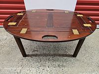 Oval wooden butler tray on stand showing top surface, brass hinges and cutout handles