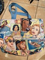 Front view of tote bag showing full pop-art comic graphic exterior and blue handles