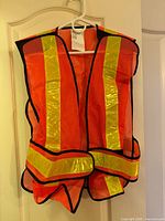 Front view of orange high-visibility vest with reflective stripes on hanger