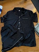 Black satin pyjama set laid flat showing piping detail, top and shorts visible