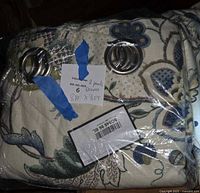 Folded floral curtain panel in plastic wrap showing metal grommets and size note