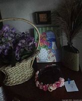 Overall lot showing basket with flowers, signed painting, vase with faux grass, headphones